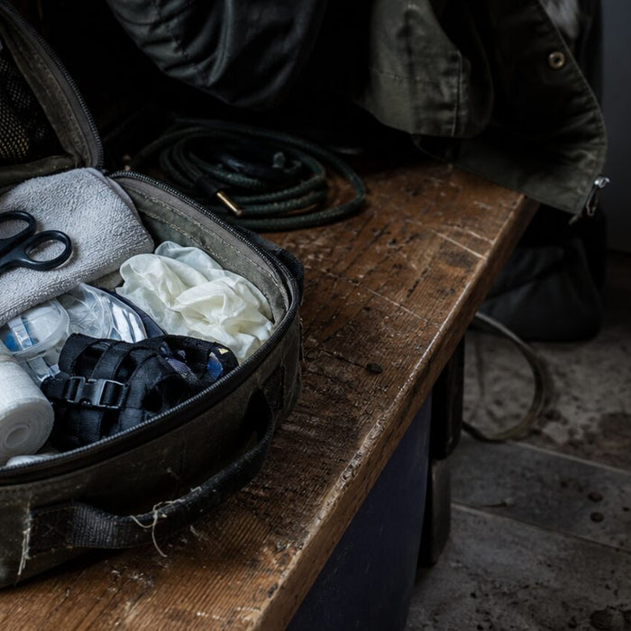 A calm dog rests beside an open red fabric first aid bag holding plain, unbranded emergency supplies.