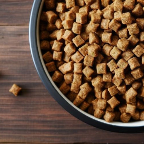 Top view of a black and white bowl of brown dry dog kibble on a dark wood table with a few loose pieces scattered around it