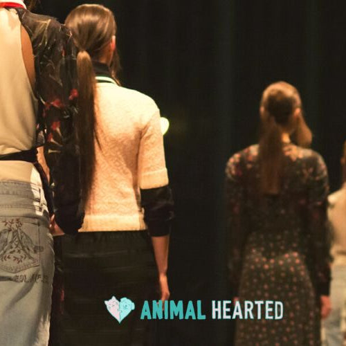 Models seen from behind walking in a line on a dark runway