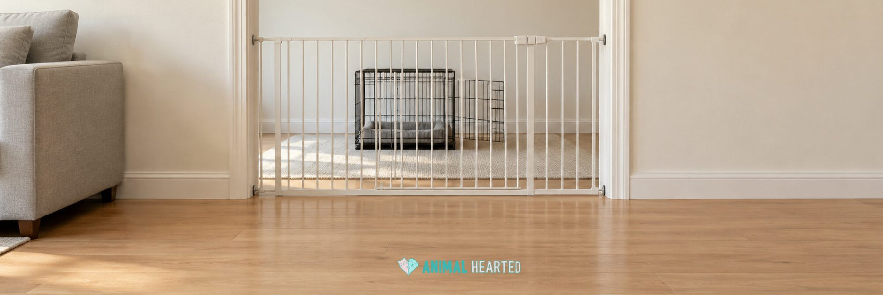 A white baby gate across a living room doorway with an open wire dog crate and a gray cushion on the far side, on a light wood floor