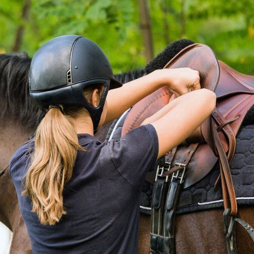 woman securing saddle on a horse
